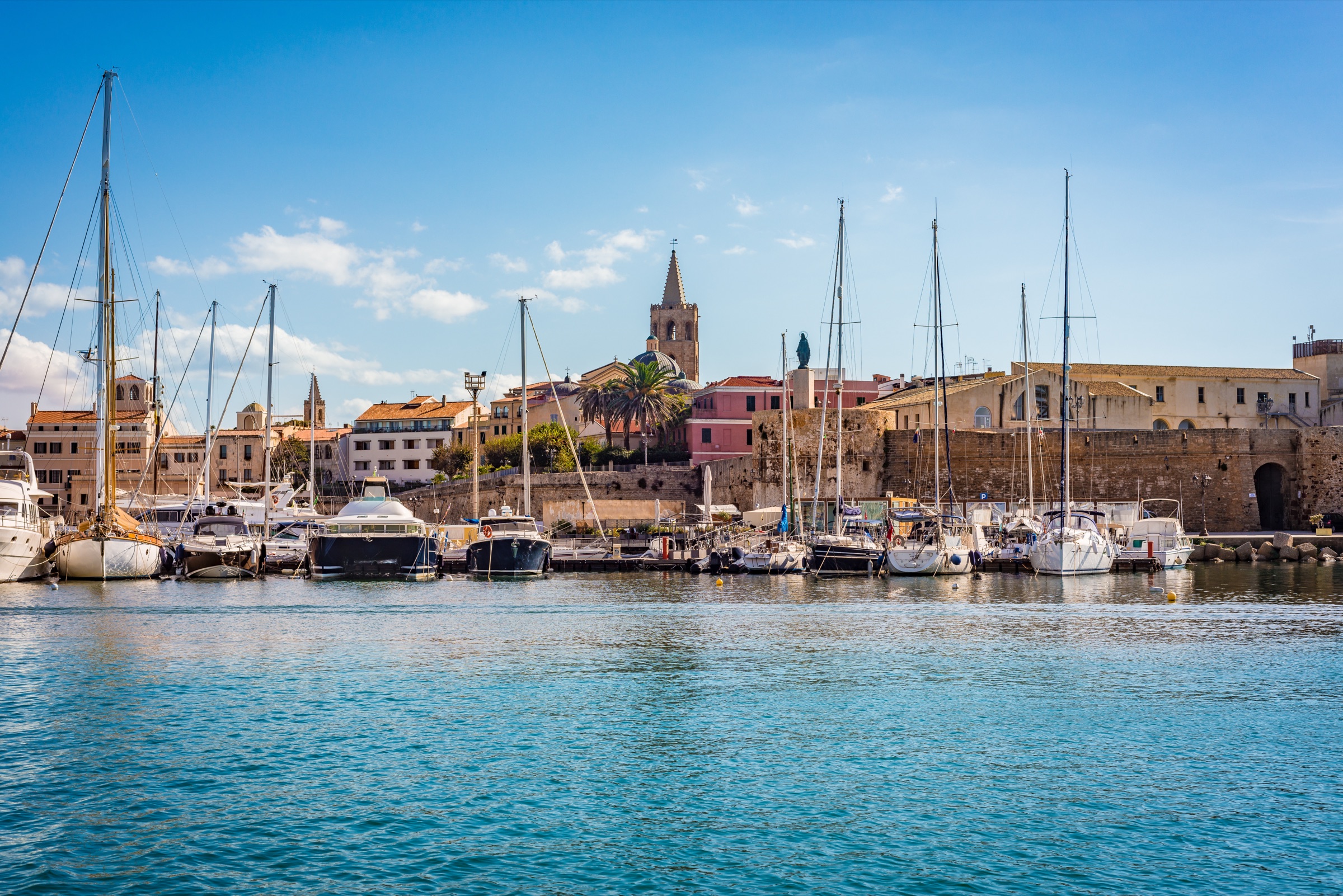 Sailboats in Alghero's old harbour, with the cathedral bell tower behind