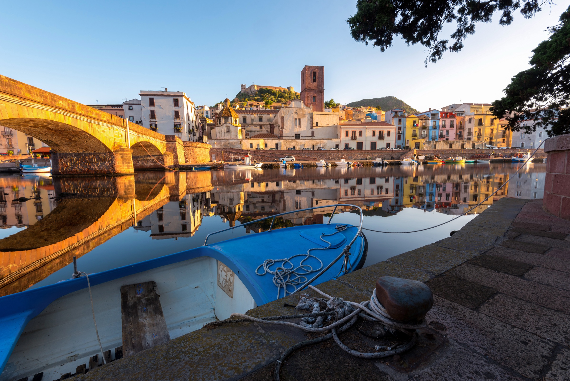 Bosa at golden hour, with pastel houses reflected in the Temo river and the castle on the hill