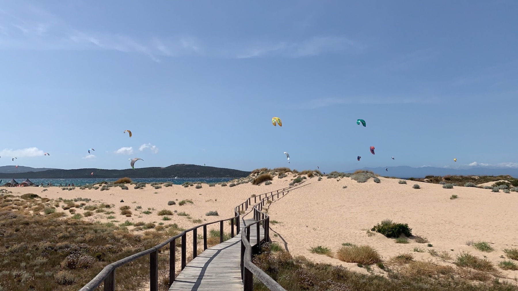 Wooden boardwalk leading down to Porto Pollo beach with kites filling the sky