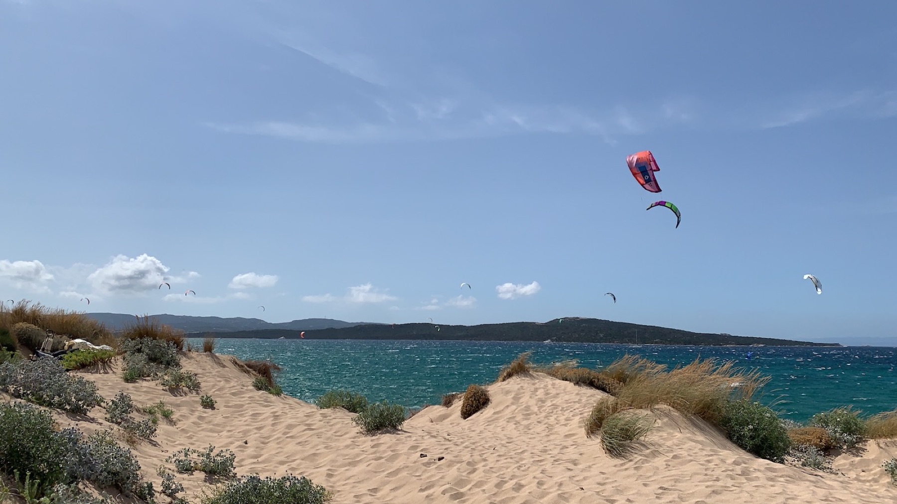 Kitesurfers in flight above Porto Pollo's dunes, with Isola dei Gabbiani in the background