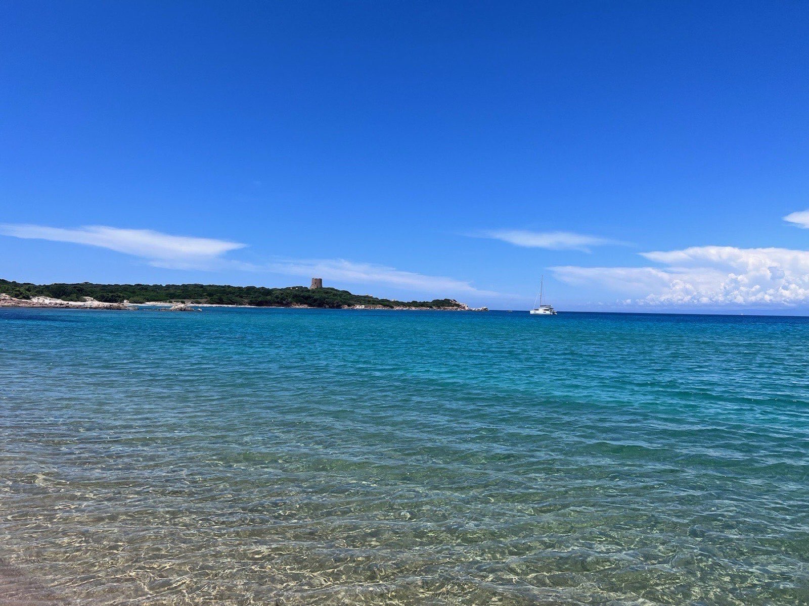 Clear turquoise water at Vignola Mare beach, with the tower on the headland