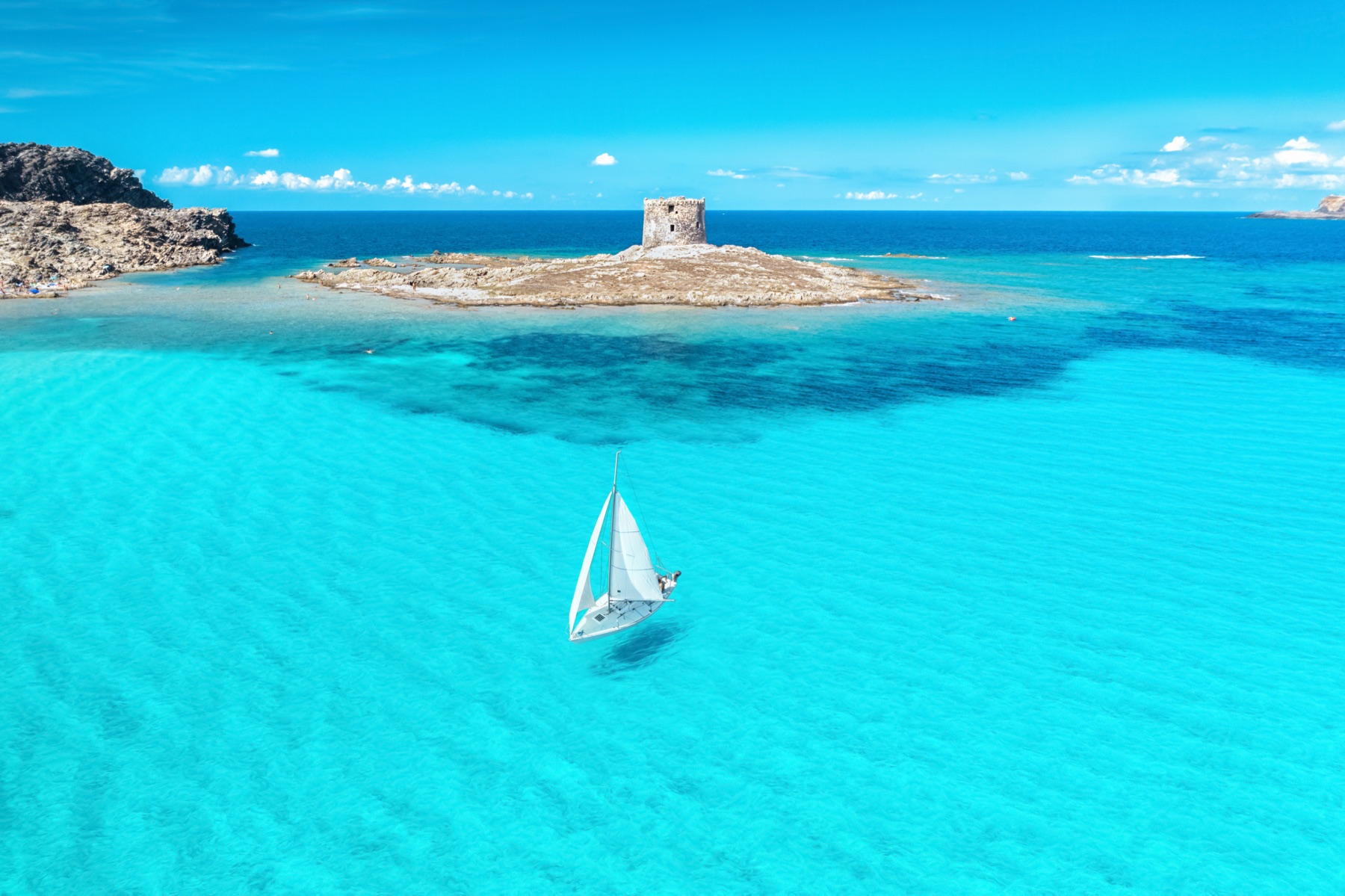 Aerial of La Pelosa beach with a white sailing yacht and the Aragonese tower